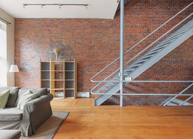 unfurnished living room featuring track lighting, baseboard heating, wood finished floors, and brick wall