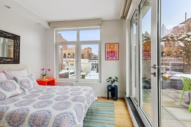 bedroom with light wood-type flooring, multiple windows, a city view, and access to outside