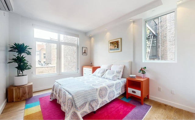 bedroom with a wall unit AC, multiple windows, and light hardwood / wood-style flooring