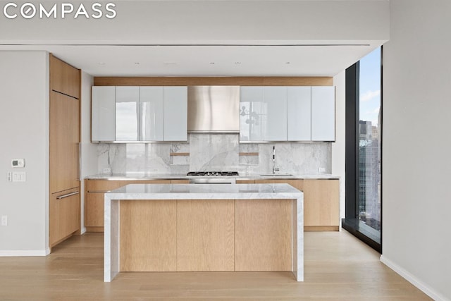 kitchen with tasteful backsplash, sink, white cabinetry, expansive windows, and light wood-type flooring