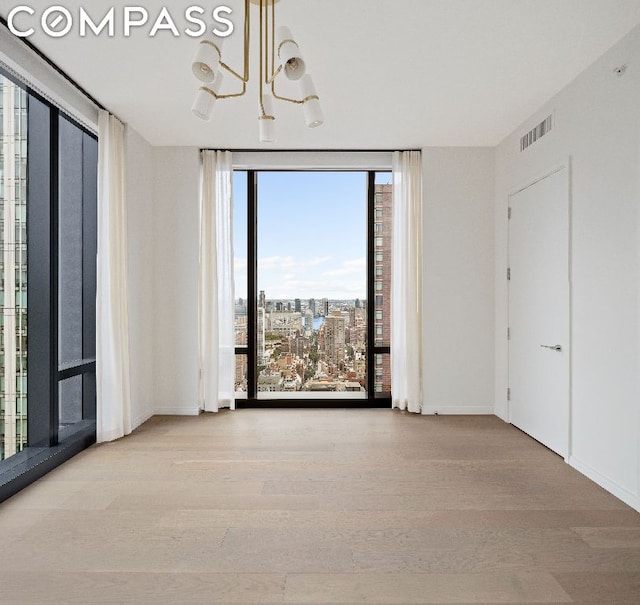 unfurnished room with expansive windows, light wood-type flooring, and an inviting chandelier