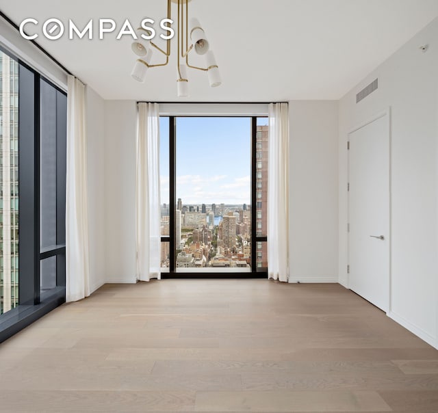 empty room featuring a city view, wood finished floors, visible vents, baseboards, and expansive windows