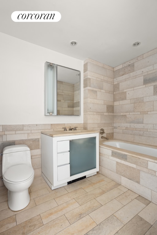 bathroom with toilet, tile walls, tiled bath, and vanity