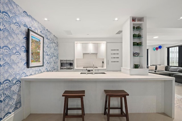 kitchen featuring white cabinetry, sink, stainless steel microwave, and a kitchen breakfast bar