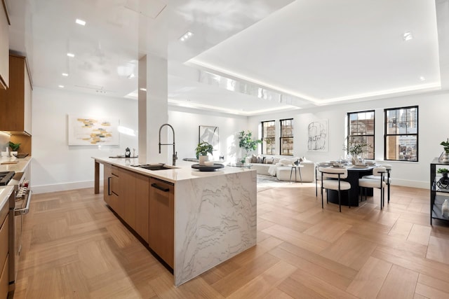 kitchen featuring a center island with sink, appliances with stainless steel finishes, modern cabinets, a raised ceiling, and a sink