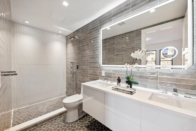 bathroom featuring toilet, a sink, tile walls, double vanity, and tiled shower