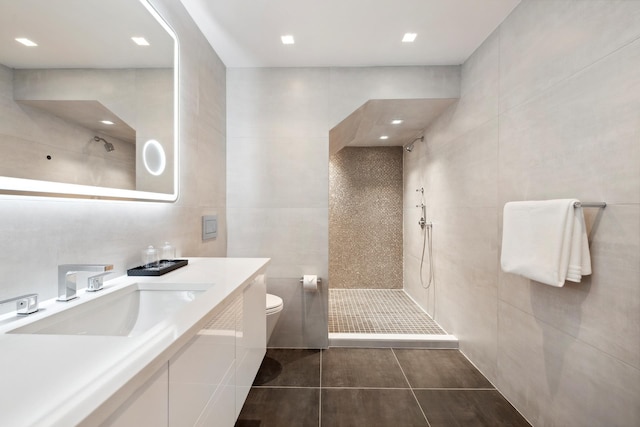 bathroom with tile patterned flooring, toilet, vanity, tiled shower, and tile walls