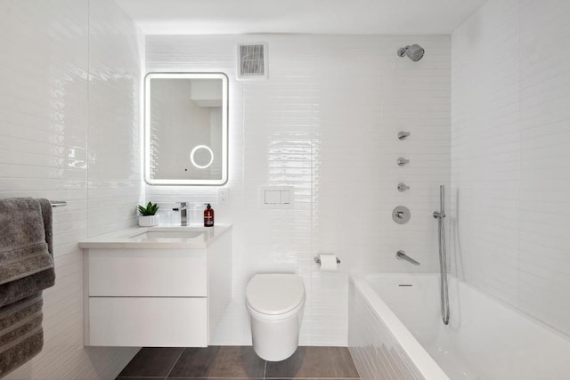 full bathroom featuring tiled shower / bath, vanity, toilet, and tile walls