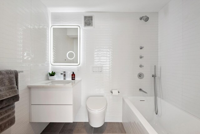 bathroom with toilet, tile walls, vanity, and tiled shower / bath