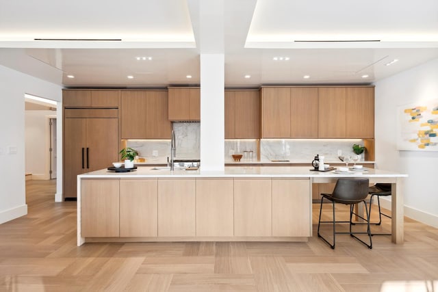 kitchen featuring a sink, light countertops, a large island, modern cabinets, and tasteful backsplash