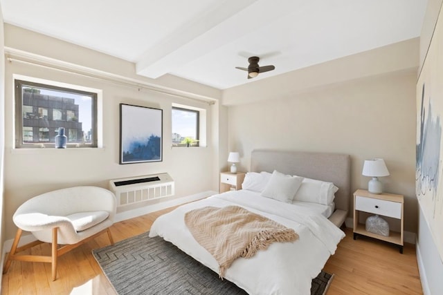 bedroom featuring ceiling fan, light hardwood / wood-style flooring, beamed ceiling, and a wall mounted air conditioner