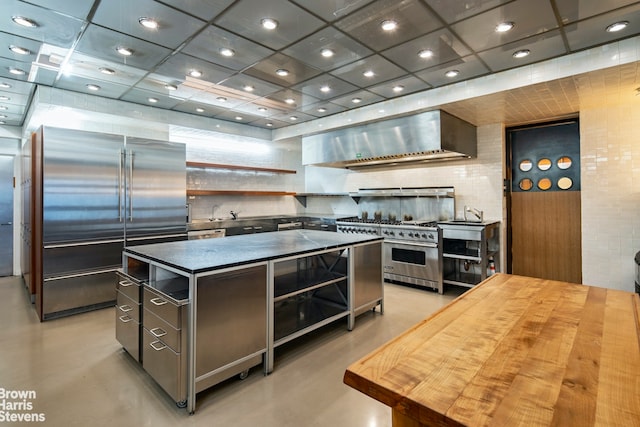 kitchen featuring a paneled ceiling, premium appliances, a kitchen island, beverage cooler, and wall chimney range hood