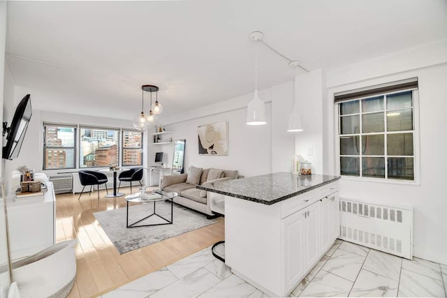 kitchen with white cabinets, radiator heating unit, a kitchen bar, dark stone countertops, and hanging light fixtures