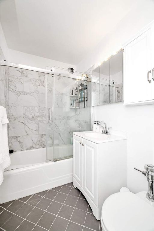 full bathroom featuring combined bath / shower with glass door, vanity, tile patterned floors, and toilet