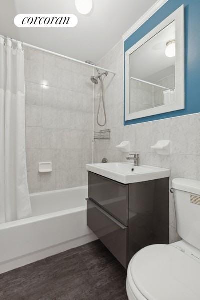 bathroom with toilet, wood finished floors, shower / bath combo with shower curtain, vanity, and tile walls