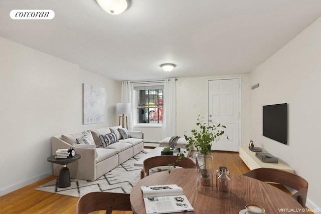 living area featuring a baseboard heating unit, wood finished floors, visible vents, and baseboards