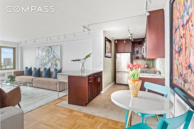 kitchen with rail lighting, appliances with stainless steel finishes, open shelves, open floor plan, and a peninsula