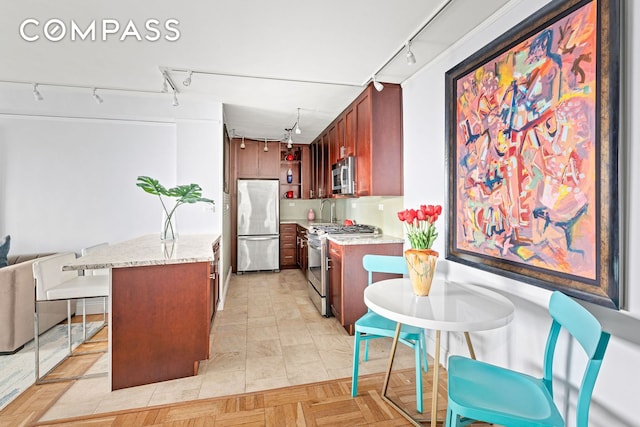 kitchen featuring stainless steel appliances, rail lighting, a sink, light stone countertops, and open floor plan
