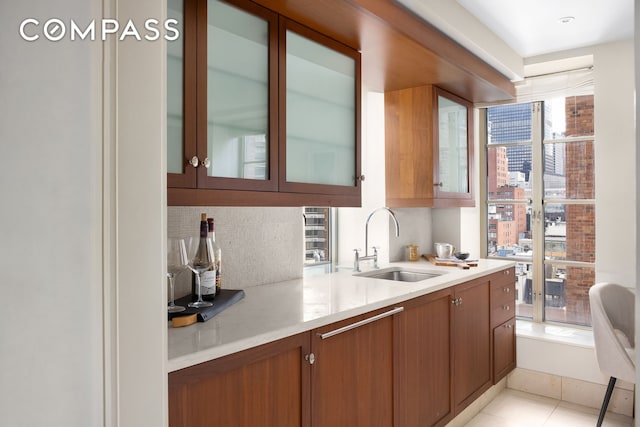 kitchen featuring light tile patterned floors, brown cabinetry, a sink, light countertops, and backsplash