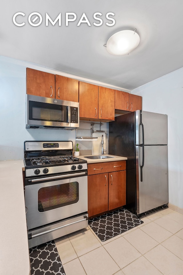 kitchen with appliances with stainless steel finishes, light countertops, a sink, and light tile patterned floors