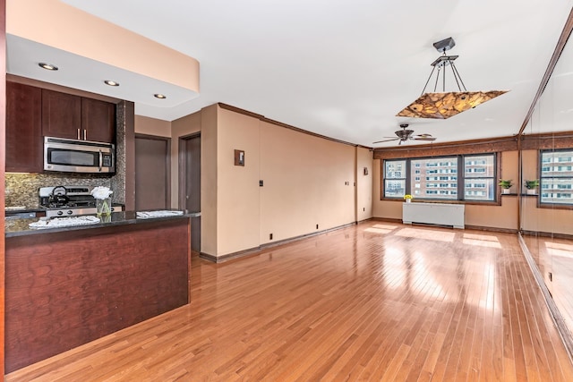 kitchen with pendant lighting, light wood-style flooring, radiator heating unit, appliances with stainless steel finishes, and dark brown cabinets