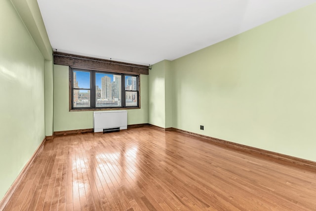 unfurnished room featuring radiator, a city view, baseboards, and light wood finished floors