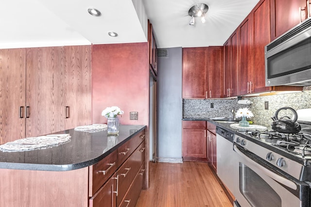 kitchen featuring reddish brown cabinets, light wood finished floors, dark stone counters, decorative backsplash, and stainless steel appliances