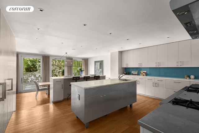 kitchen featuring tasteful backsplash, visible vents, a kitchen island with sink, light wood-type flooring, and white cabinetry