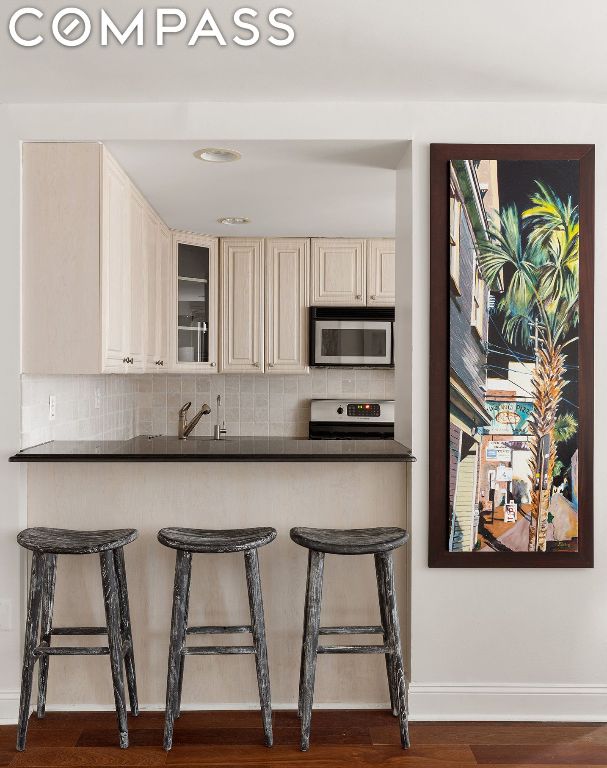 kitchen with sink, a breakfast bar, appliances with stainless steel finishes, dark hardwood / wood-style flooring, and decorative backsplash