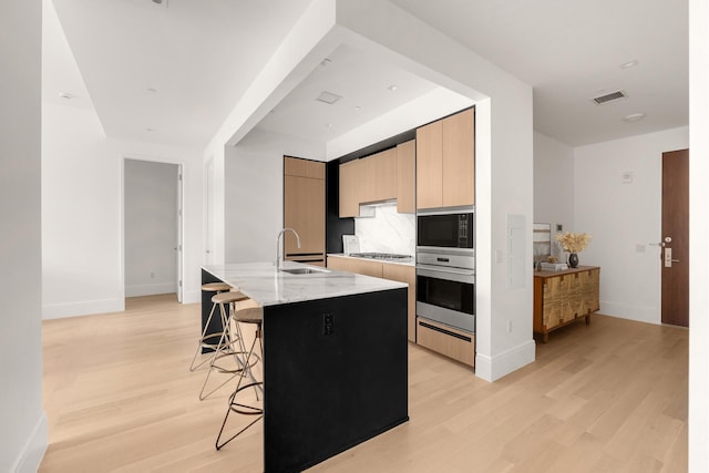 kitchen featuring light stone counters, stainless steel appliances, a breakfast bar, visible vents, and an island with sink