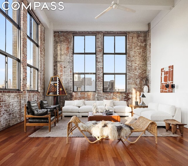 living area featuring wood-type flooring, brick wall, and ceiling fan