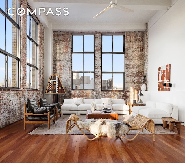 living area featuring wood-type flooring, brick wall, and ceiling fan