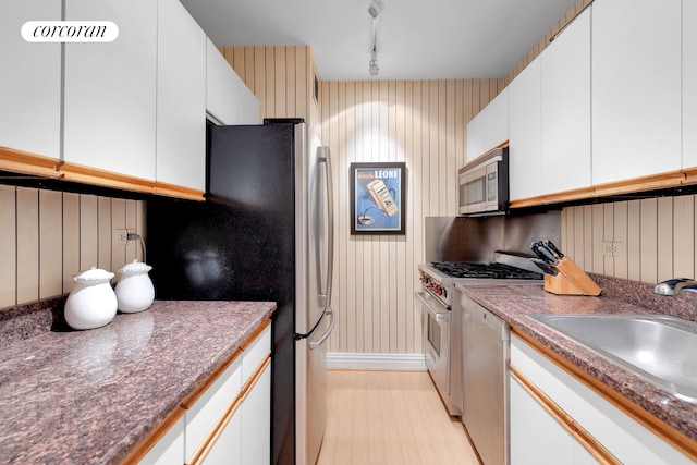 kitchen with a sink, light wood-type flooring, appliances with stainless steel finishes, and white cabinetry