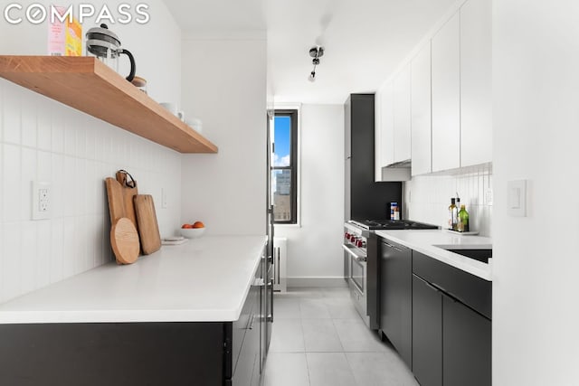 kitchen featuring light tile patterned floors, stainless steel range, backsplash, and white cabinets