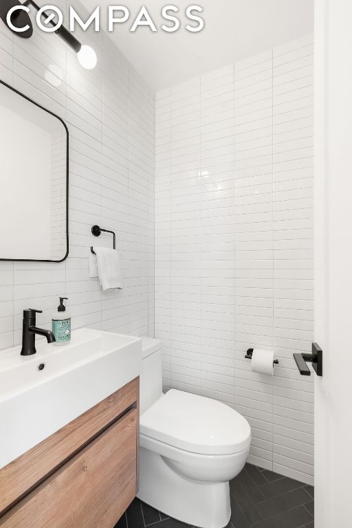 bathroom with toilet, tile walls, tile patterned floors, and vanity