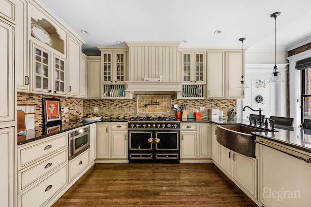 kitchen with dark wood-style floors, cream cabinetry, dark countertops, decorative backsplash, and a sink