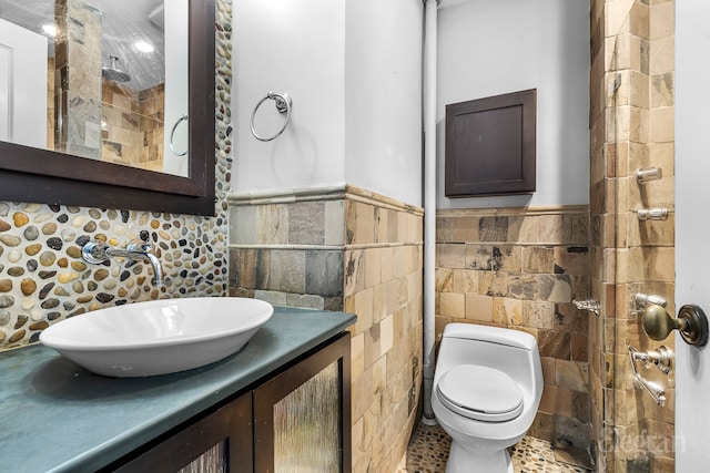 bathroom with a wainscoted wall, tile walls, toilet, a tile shower, and vanity