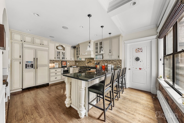 kitchen featuring premium appliances, cream cabinetry, a baseboard radiator, dark countertops, and wood finished floors