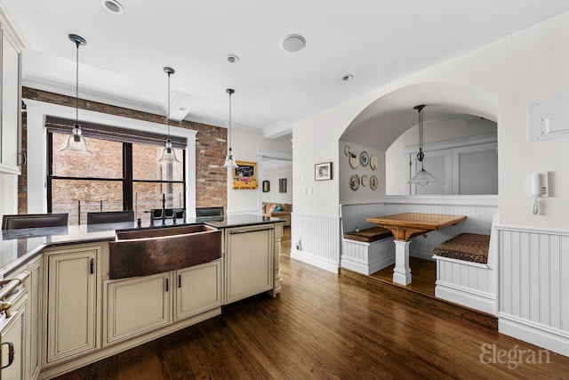 kitchen with wainscoting, dark wood-style floors, cream cabinets, pendant lighting, and a sink