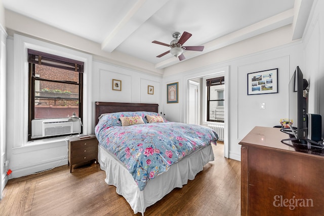 bedroom featuring beam ceiling, a decorative wall, radiator heating unit, ceiling fan, and wood finished floors