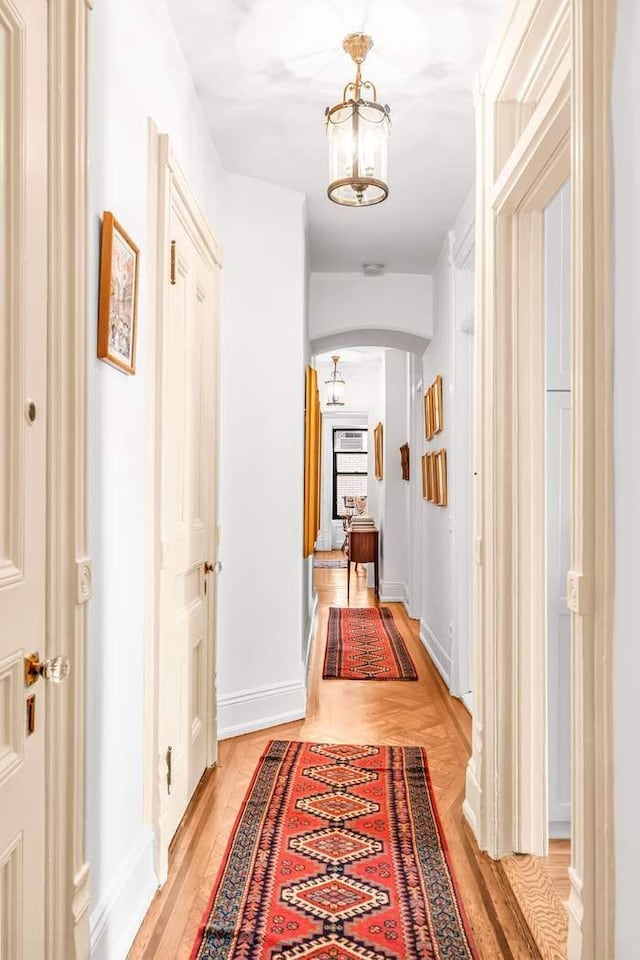 hall with light wood-style floors, arched walkways, a notable chandelier, and baseboards