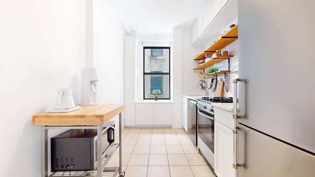 kitchen with light tile patterned flooring, stainless steel gas stove, white cabinetry, dishwashing machine, and white fridge