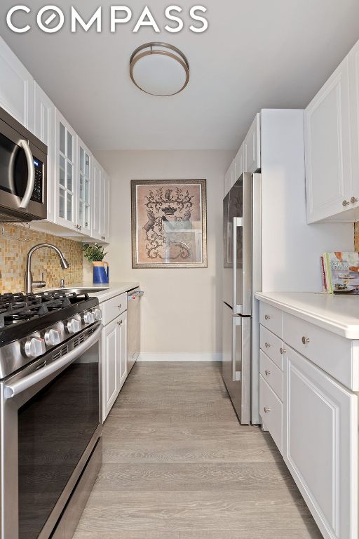 kitchen with tasteful backsplash, stainless steel appliances, light hardwood / wood-style floors, and white cabinets