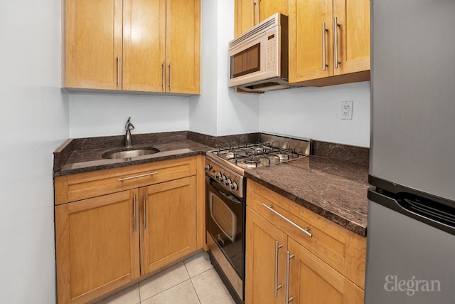 kitchen featuring light tile patterned floors, appliances with stainless steel finishes, dark stone counters, and sink