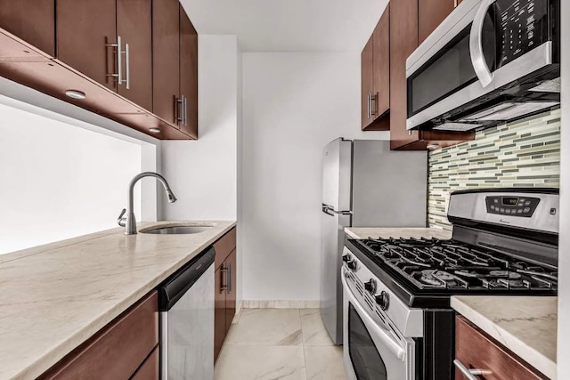 kitchen with light stone counters, a sink, baseboards, appliances with stainless steel finishes, and backsplash