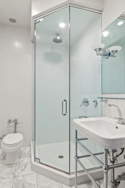 bathroom featuring toilet, tile walls, and a shower with door