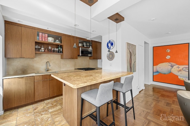 kitchen featuring glass insert cabinets, appliances with stainless steel finishes, light countertops, pendant lighting, and a sink