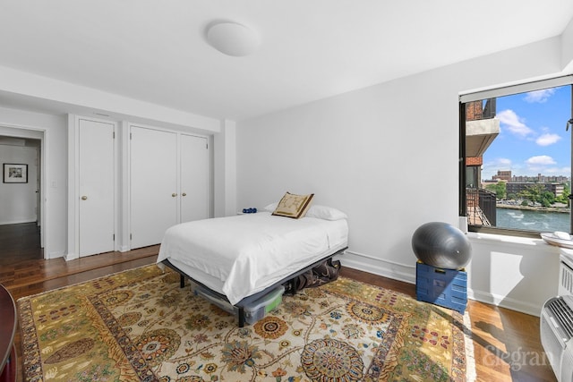 bedroom featuring dark wood-style floors, a closet, a water view, and baseboards