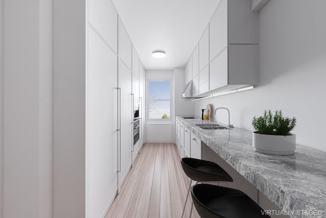 kitchen with a sink, light wood-style floors, white cabinets, range hood, and modern cabinets