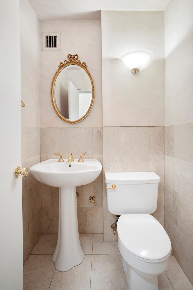 half bath with tile walls, toilet, and visible vents